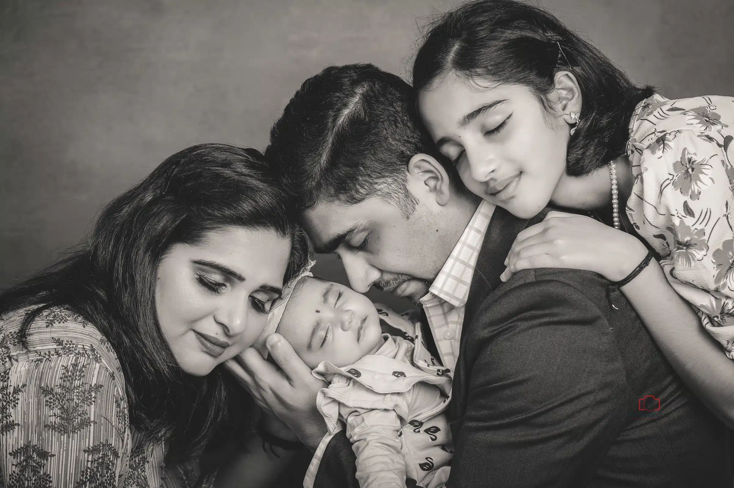 Emotional black and white family portrait featuring parents and two daughters lovingly embracing their newborn baby during a professional family photography session by Ruchika Jain Photography in Wellington.